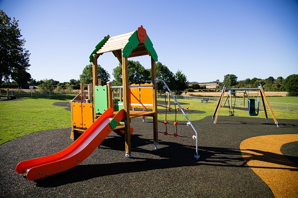 A slide and climbing apparatuses with a swing set in the background at the Swinburne playground 