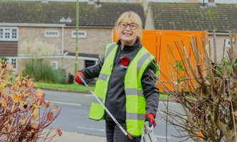 A Settle colleague standing in a residential area wearing a high-vis jacket and holding a litter picker and a waste bag.