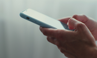 Close-up of a person's hands holding and using a smartphone with a light blue case, against a softly blurred background.