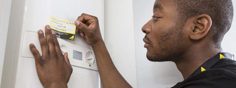 Person placing a yellow sticker on a white boiler unit with two dials and a small display screen.