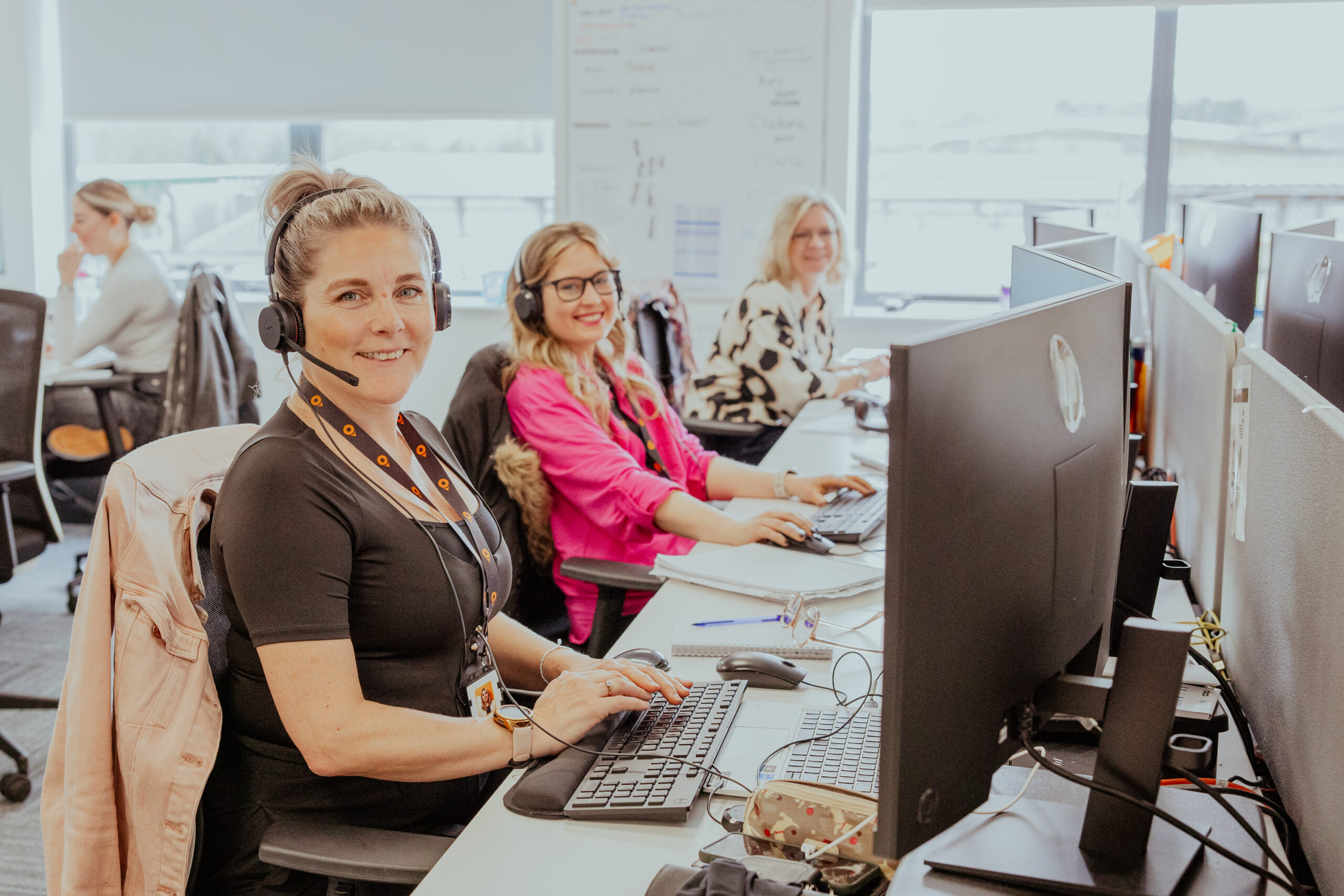 Three people working at desks with computers in a bright office setting.