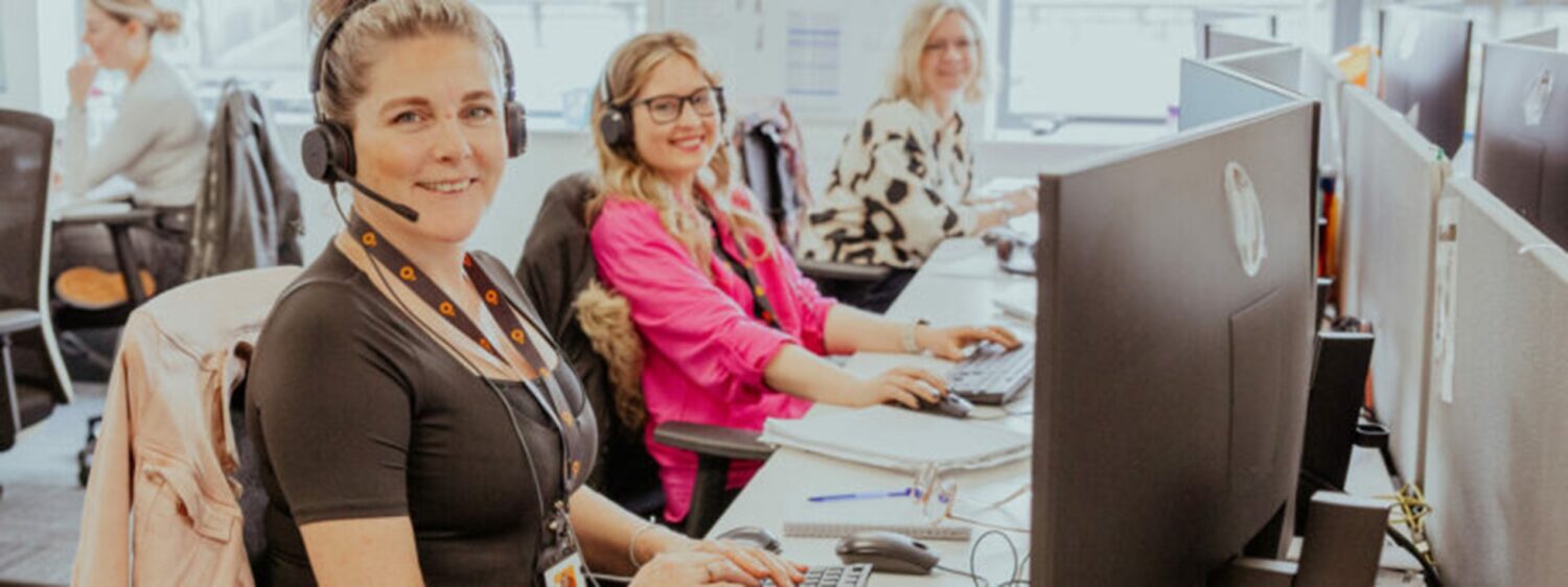 Three people working at desks with computers in a bright office setting.